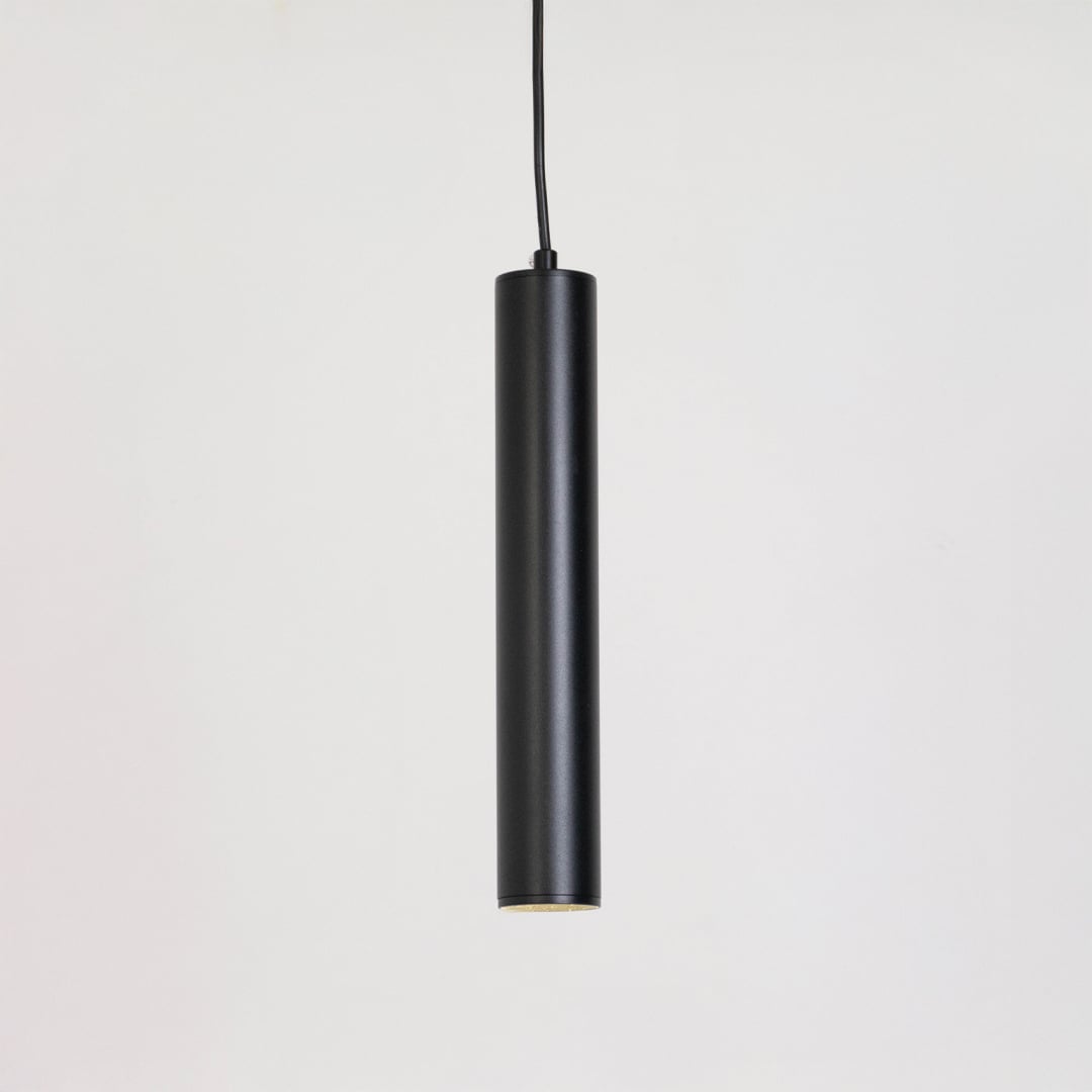 Black tubular pendant light glowing softly on a white background showing focused downward illumination.