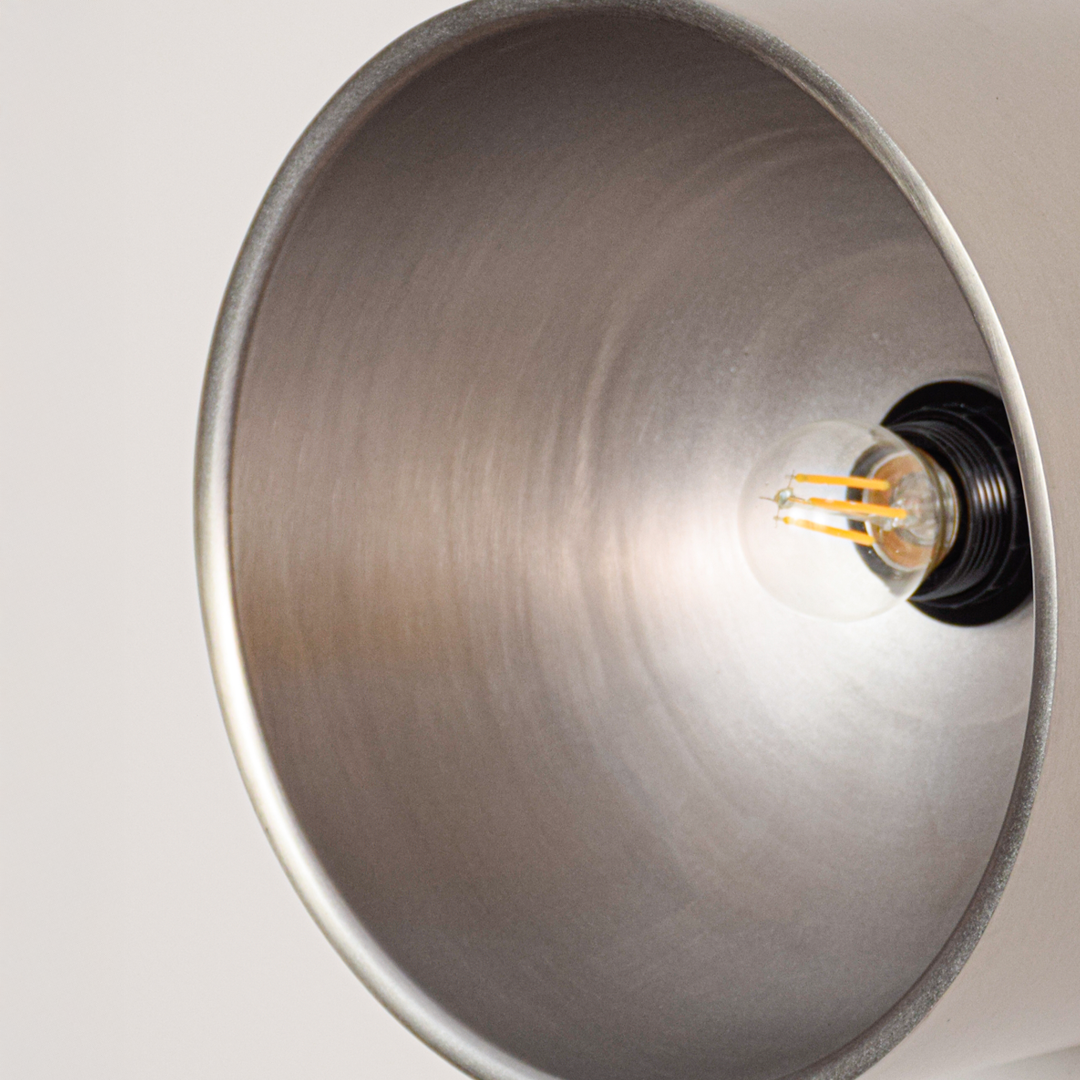 Closeup view of round wall light with exposed bulb and reflective gold interior highlighting smooth metal finish and soft warm illumination.