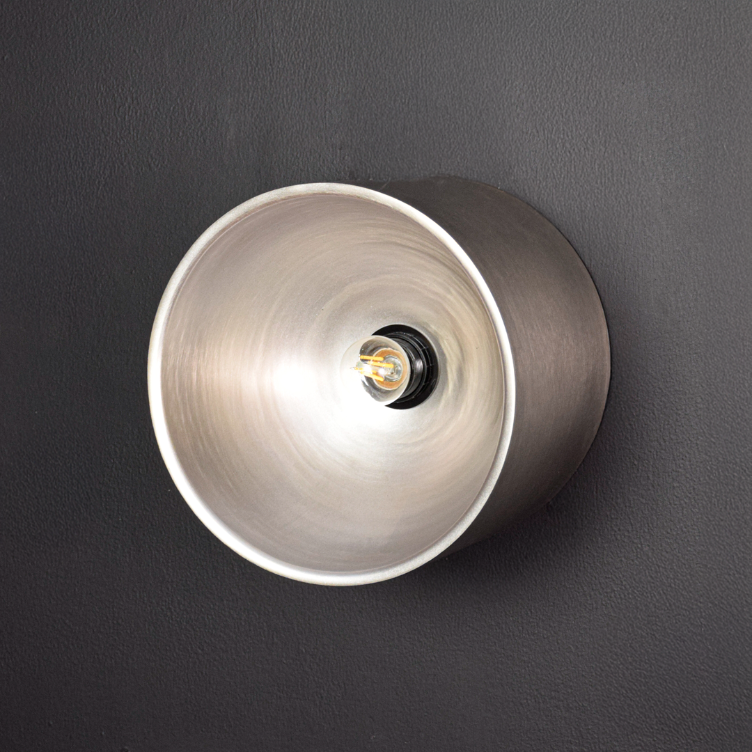 Round metal wall light switched off on dark background showing matte exterior smooth cylinder shape and centered bulb holder without illumination.