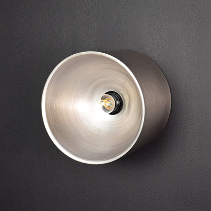 Round metal wall light switched off on dark background showing matte exterior smooth cylinder shape and centered bulb holder without illumination.