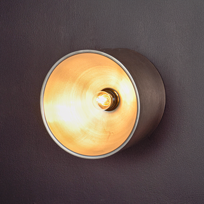 Circular wall lamp glowing on dark backdrop showing bright warm core reflective inner surface and sleek outer shell for dramatic accent lighting.