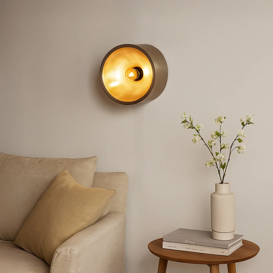 Modern round wall light glowing warmly above a beige sofa with wooden side table and vase creating a cozy living room ambience with soft ambient lighting.