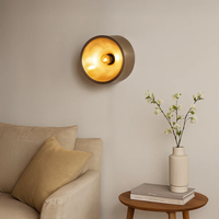 Modern round wall light glowing warmly above a beige sofa with wooden side table and vase creating a cozy living room ambience with soft ambient lighting.