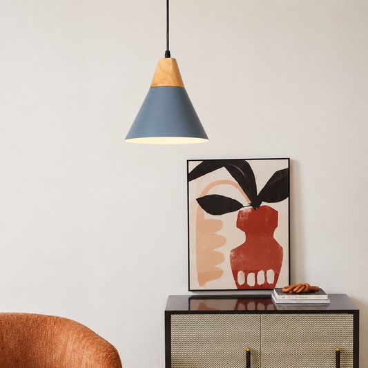 A modern pendant light with a blue-gray and natural wood shade hangs above a black cabinet in a styled interior. A framed abstract art print and a small stack of books sit on the cabinet against a light neutral wall.