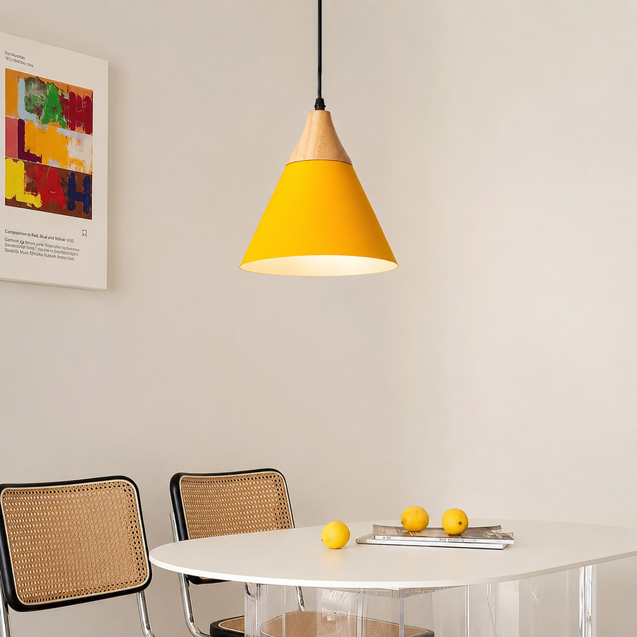 A modern pendant light with a bright yellow cone shade and a natural wood top, hanging above a white dining table with two woven-back chairs in a minimalist room.