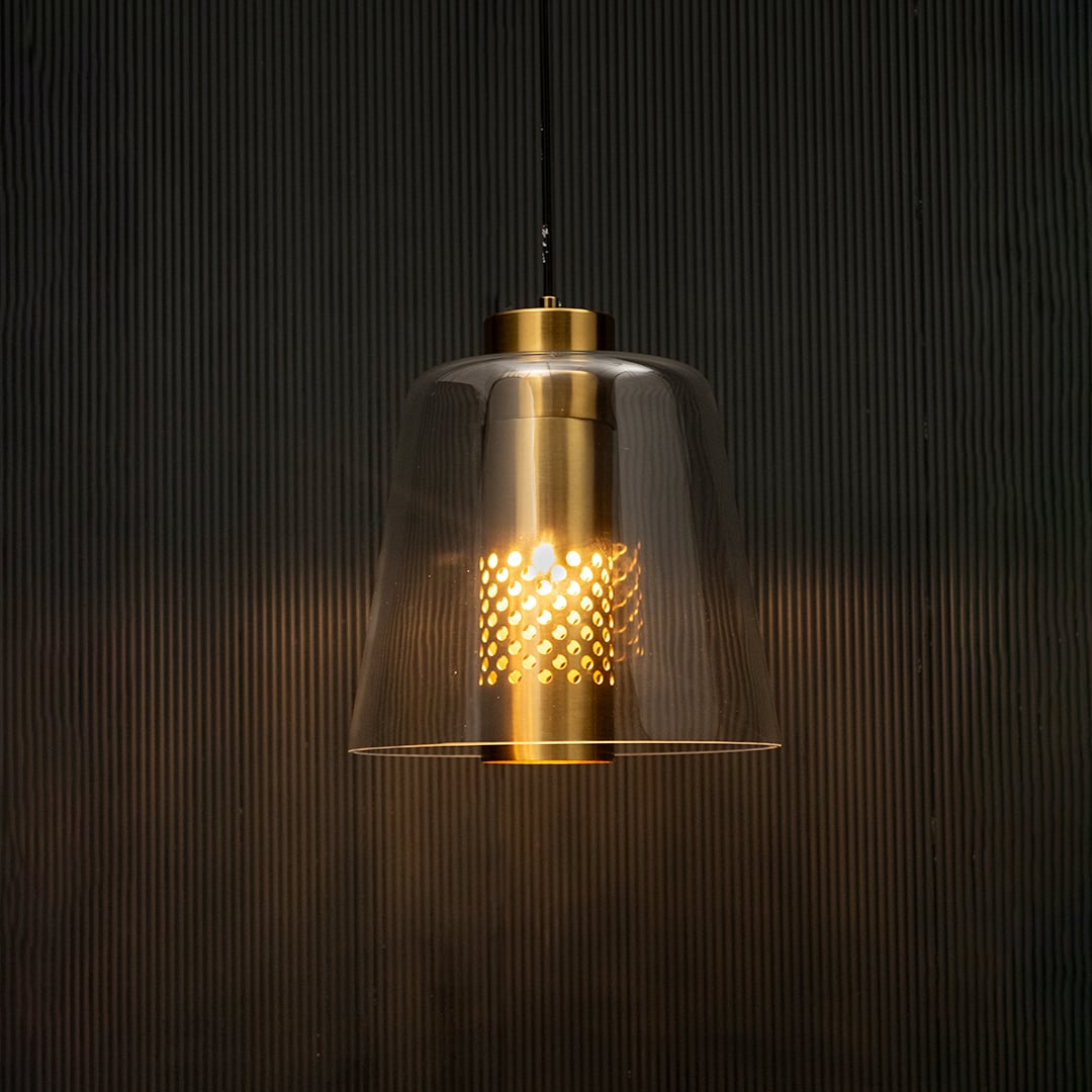 Glass pendant light with gold metal holder glowing on black background creating warm ambient lighting for modern interiors.