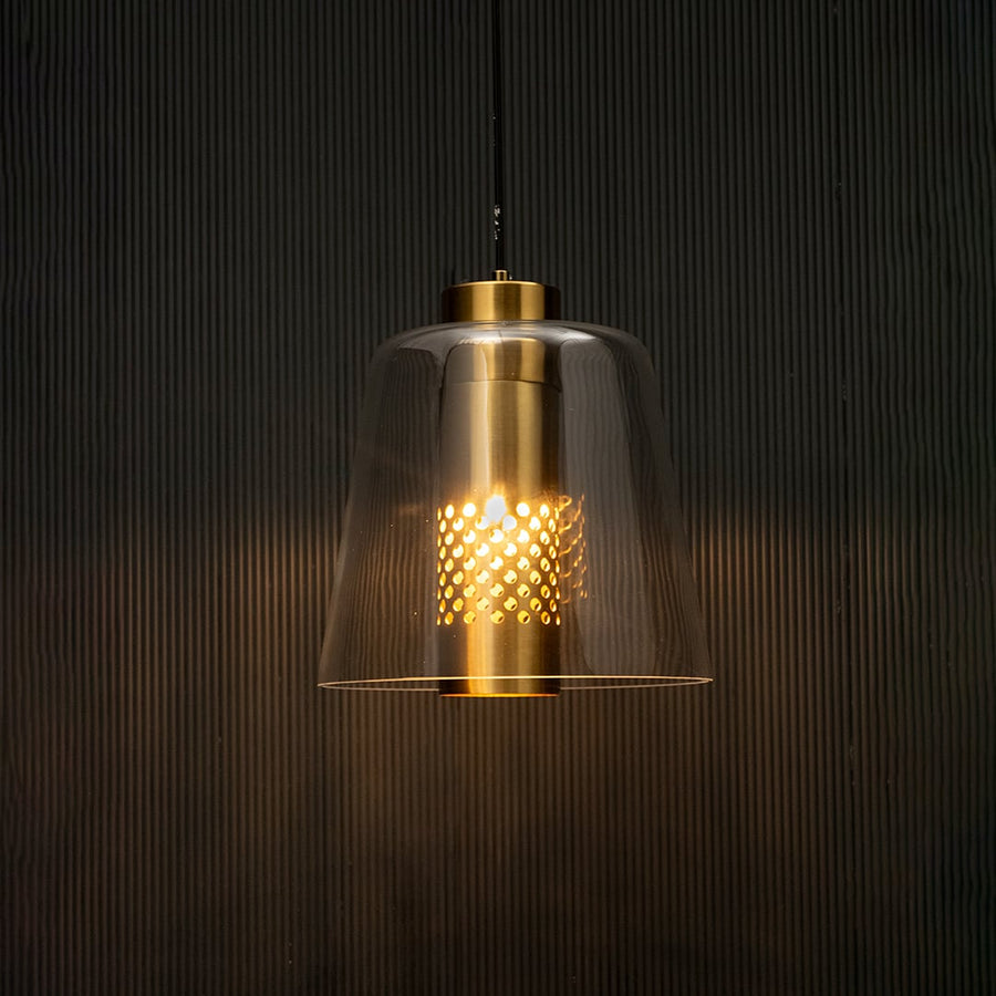 Glass pendant light with gold metal holder glowing on black background creating warm ambient lighting for modern interiors.