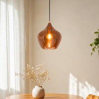 Modern copper-tinted glass teardrop pendant light hanging in a sunlit dining room over a wooden table with a ceramic flower vase.