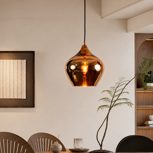 An amber glass pendant light hangs over a dining table in a warm, modern interior setting with wooden chairs and a framed wall art piece.