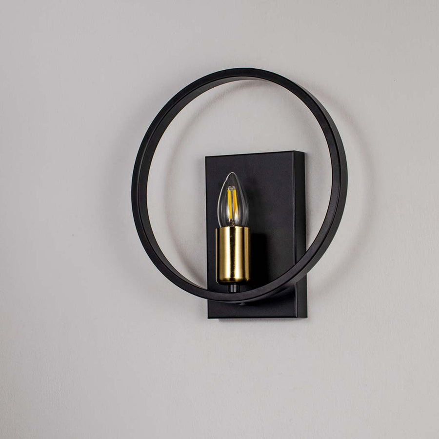 Modern wall light with matte black circular frame and gold bulb holder shown off on white background for stylish interiors.