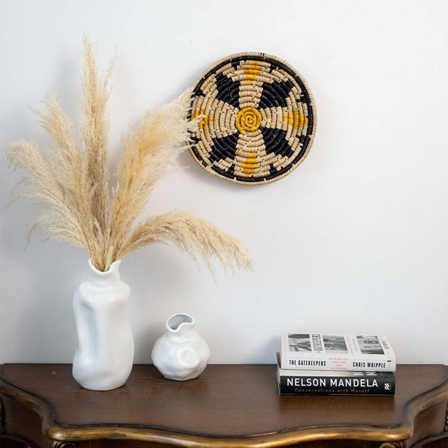 Handwoven seagrass wall basket decor in natural beige black and mustard displayed above a console creating warm boho home style.
