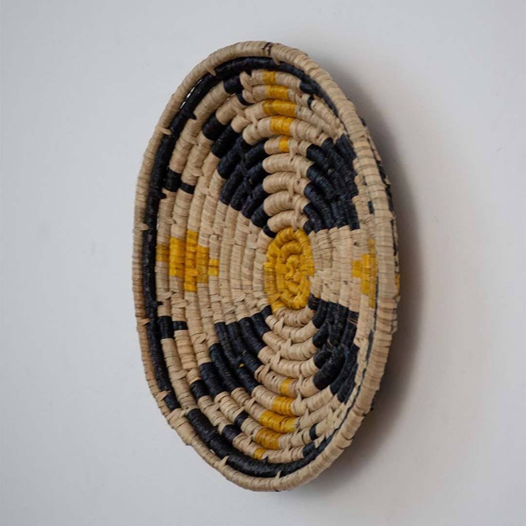 Handwoven seagrass round wall basket decor in natural beige black and mustard with raised woven profile on white background.