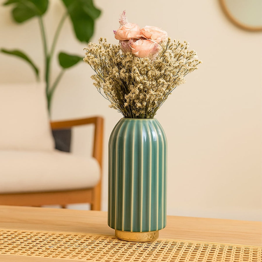 Tall green ceramic vase with gold detailing filled with pastel flowers placed on a wooden table for a modern and elegant home decor look.