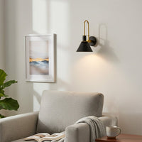Modern black metal spotlight wall light creating cozy reading corner ambiance with warm interior lighting.