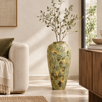 A tall, textured ceramic vase with a distressed green and gold finish, filled with dried branches, styled in a modern living room next to a beige sofa and a wooden cabinet.