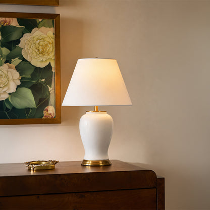 White fabric shade table lamp with ceramic white base casting warm ambient light on wooden console in luxury interior.