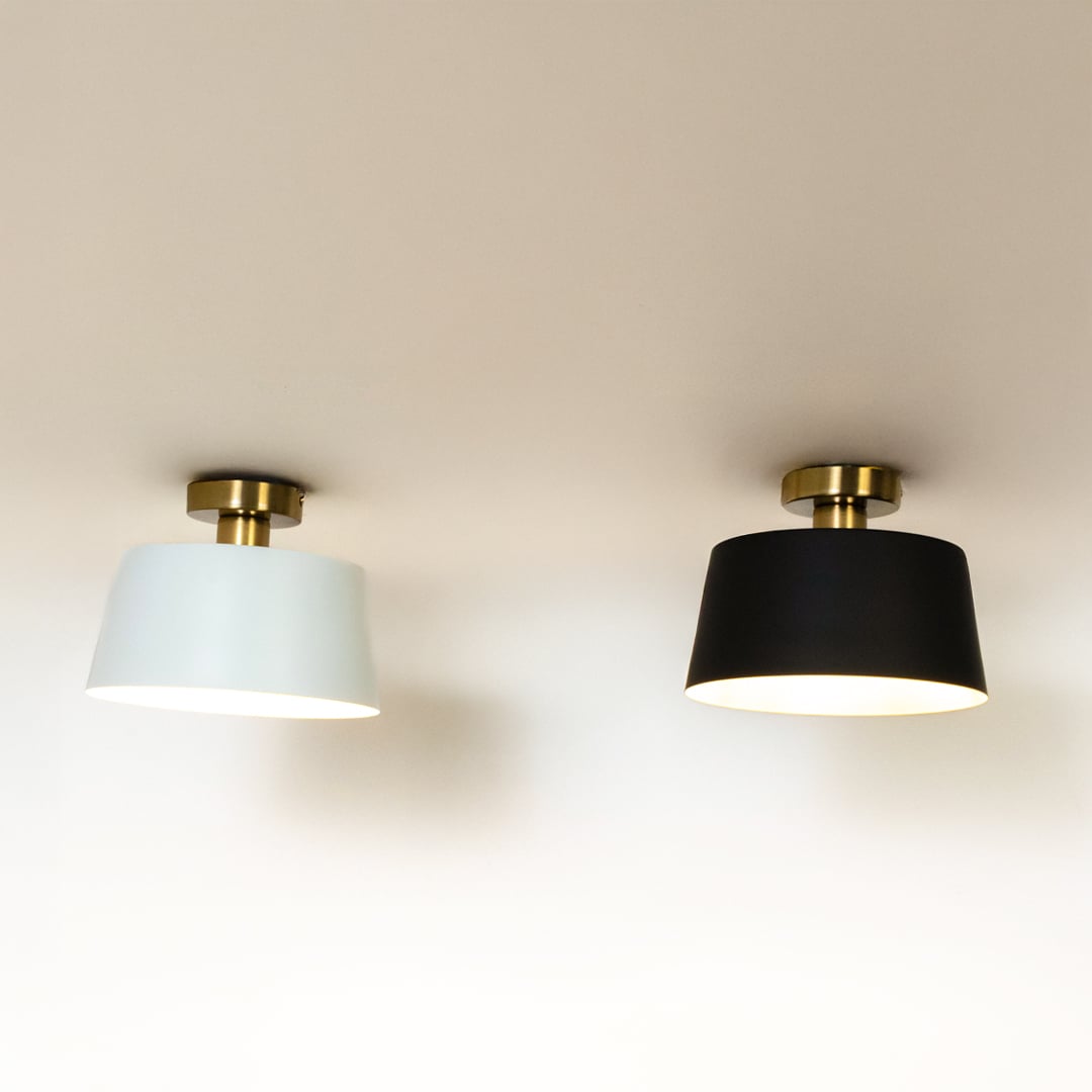 Black and white ceiling lights with gold fittings and drum shades glowing on white background for stylish modern home lighting.
