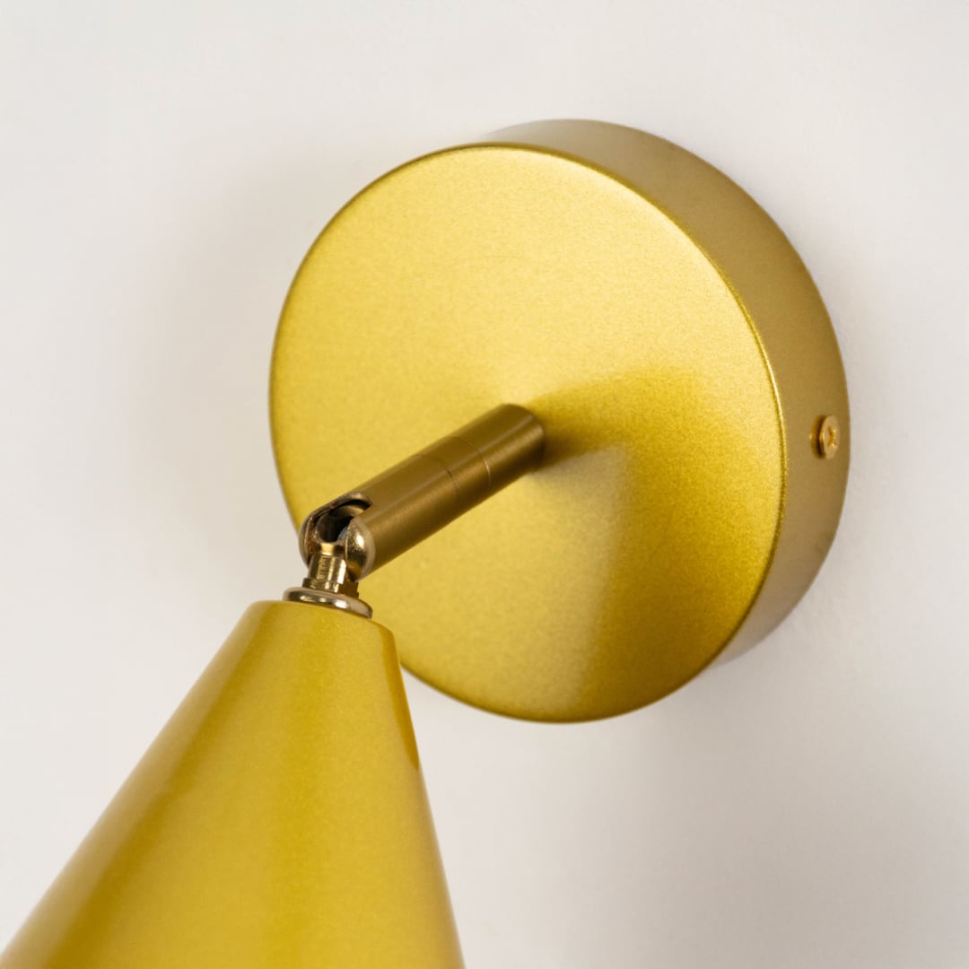 Closeup view of gold metal wall sconce highlighting its conical shade smooth metallic finish and warm lighting design suited for modern interior decor.