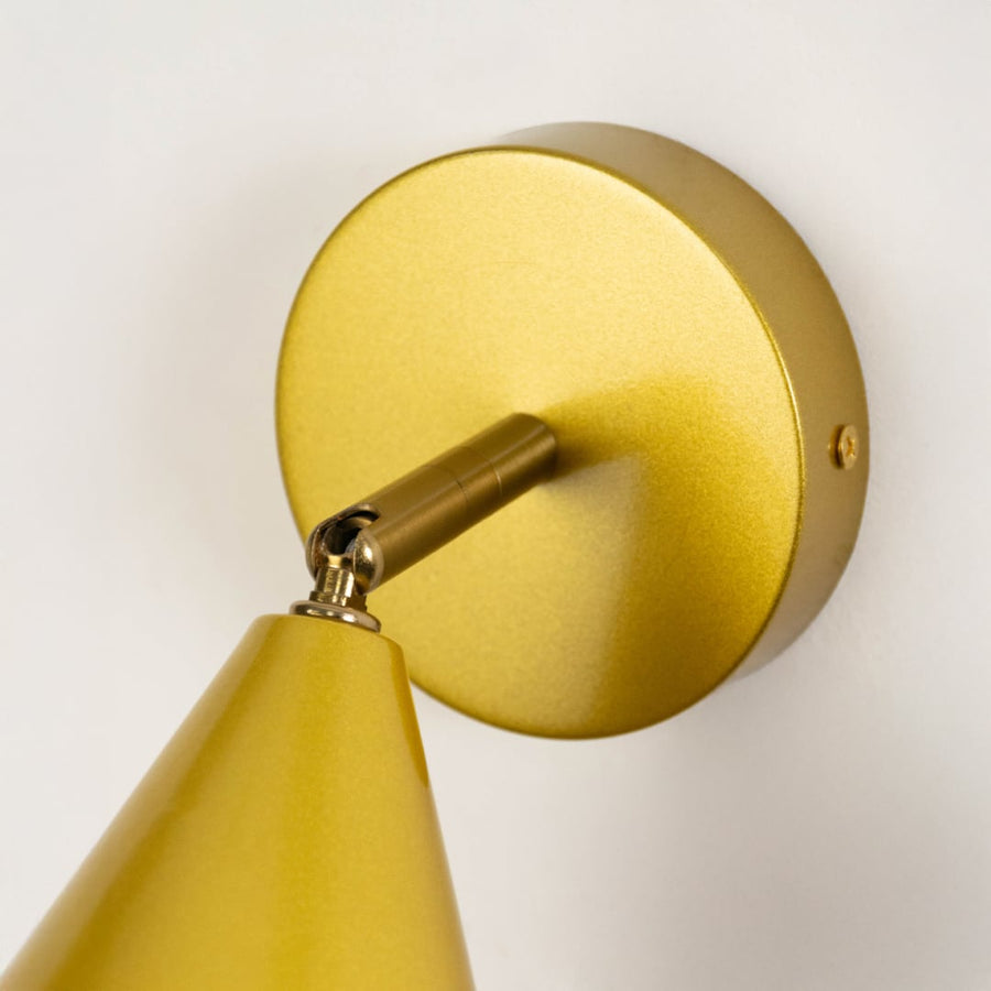 Closeup view of gold metal wall sconce highlighting its conical shade smooth metallic finish and warm lighting design suited for modern interior decor.