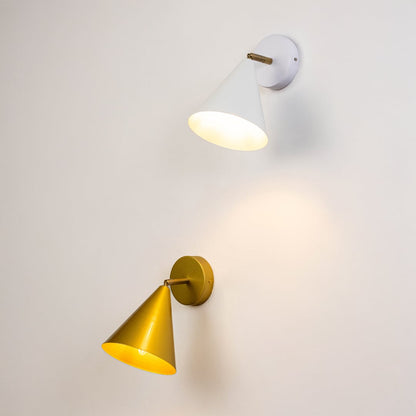 Two cone shaped wall sconces in white and gold mounted on a light wall each with a warm glowing bulb.