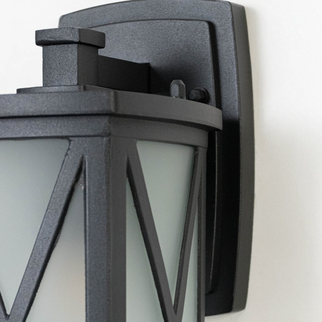 Black metal outdoor wall lantern closeup image showing textured matte frame and frosted glass with X overlay for decor.