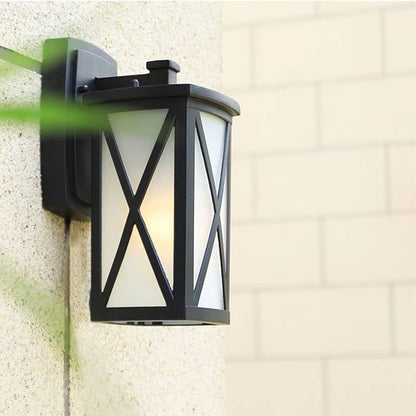 Black metal outdoor wall light lifestyle image featuring an X brace frosted glass shade mounted on a stone porch pillar.