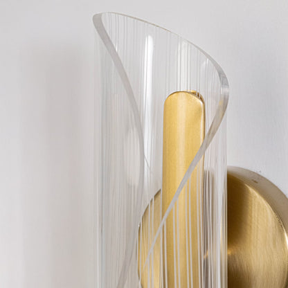 Closeup of gold wall light with sculpted clear glass shade highlighting curved textured design and premium finish.