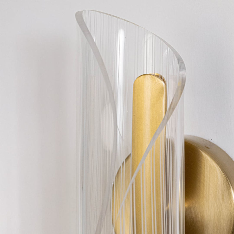 Closeup of gold wall light with sculpted clear glass shade highlighting curved textured design and premium finish.