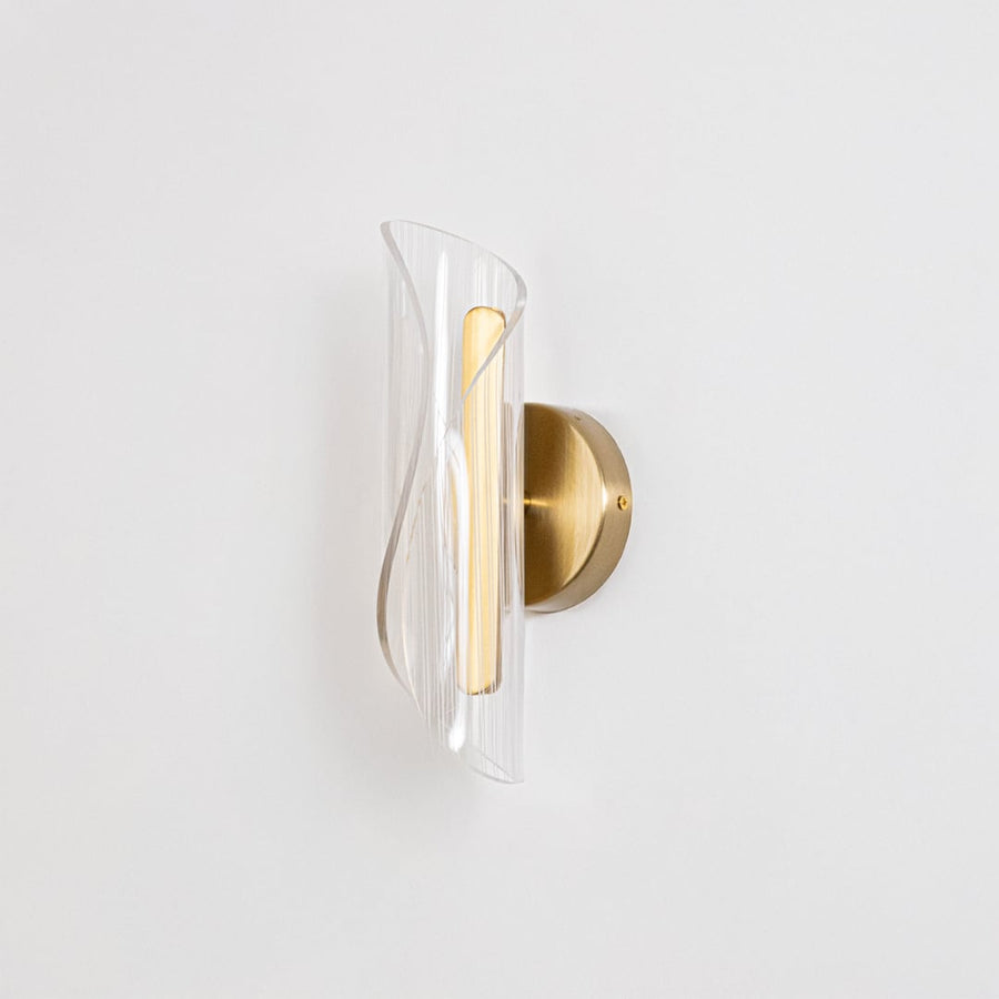 Gold wall light with sculpted clear glass shade shown on a bright white background with lights off for clarity.
