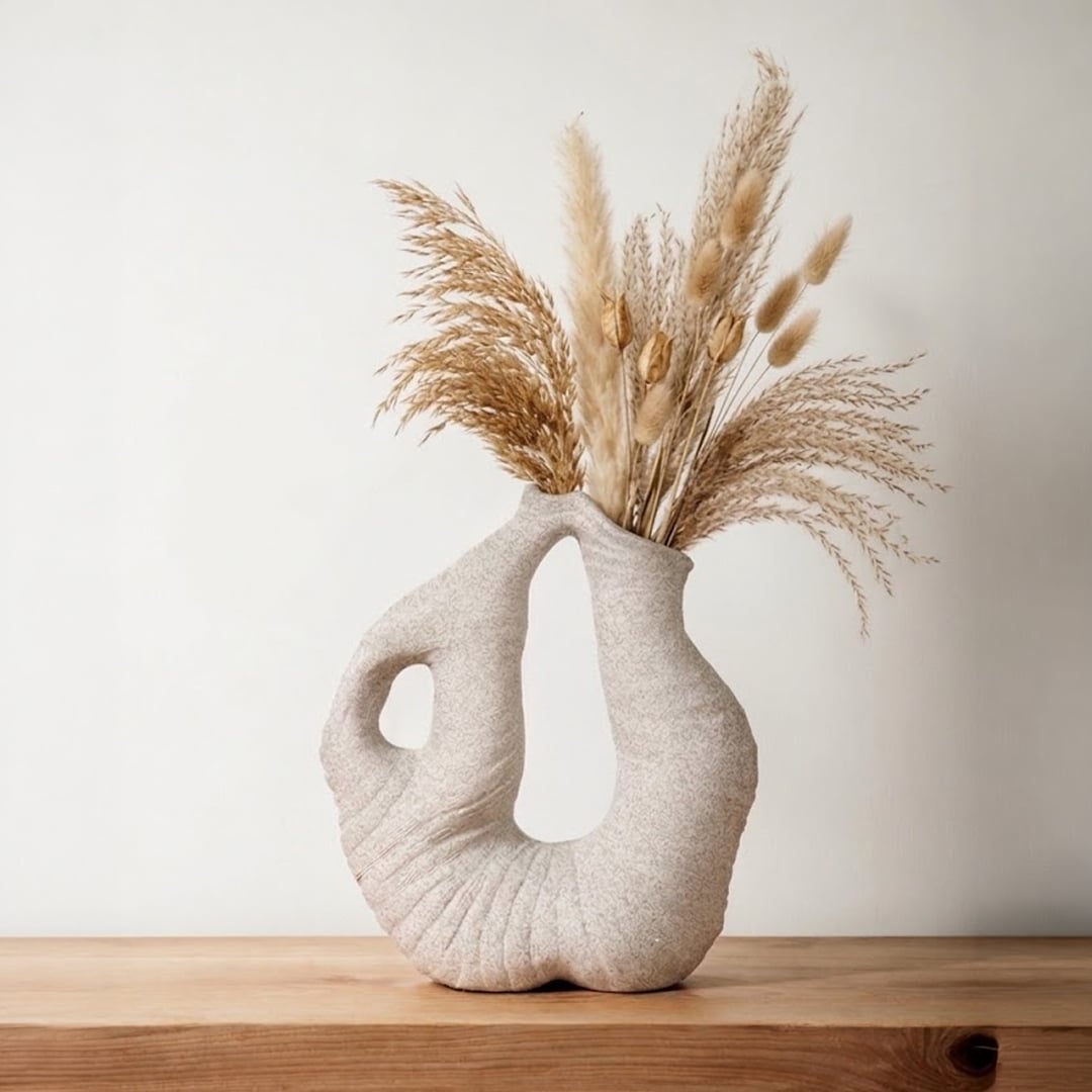 Grey sculptural ceramic vase with artistic loop design placed on outdoor table under blooming flowers creating modern charm.