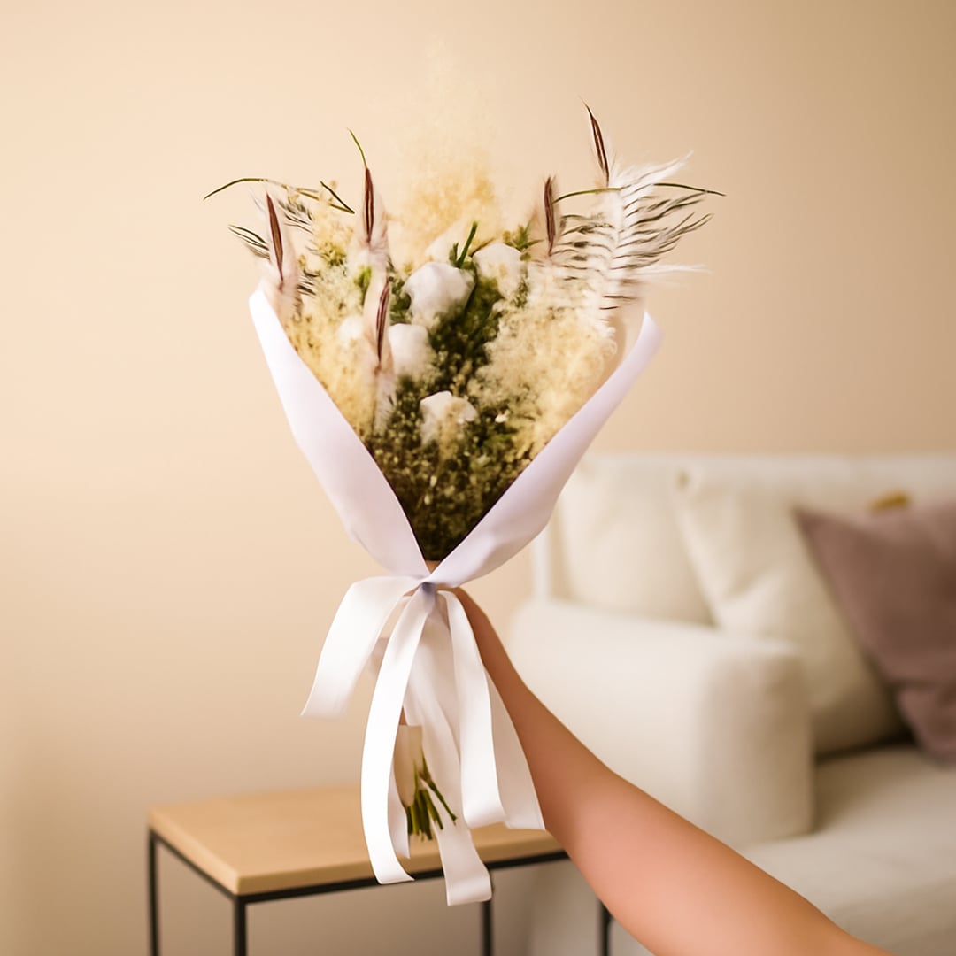 Lifestyle image showing preserved dried floral bouquet wrapped in white paper and ribbon held by hand adding soft modern home decor styling.