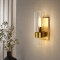 Elegant gold brass single candle wall sconce with a clear glass cylinder tube shade mounted in a luxury hallway setup.