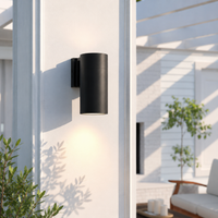 Modern black aluminum cylindrical downlight exterior wall sconce on a white stucco pillar for a contemporary patio area.