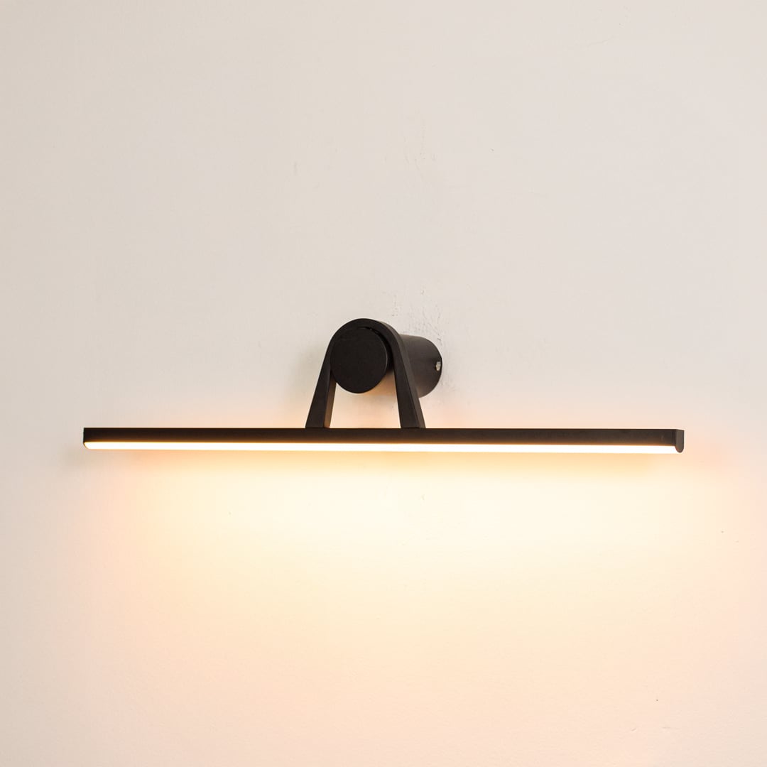 Black metal picture light switched on over white background spreading soft warm glow ideal for gallery wall lighting.