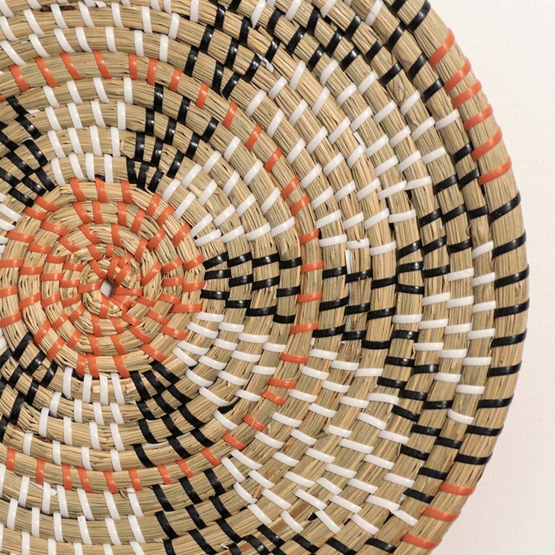 Detailed closeup of handcrafted natural seagrass wall basket with orange and black woven geometric patterns for boho decor.
