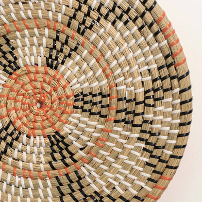 Detailed closeup of handcrafted natural seagrass wall basket with orange and black woven geometric patterns for boho decor.