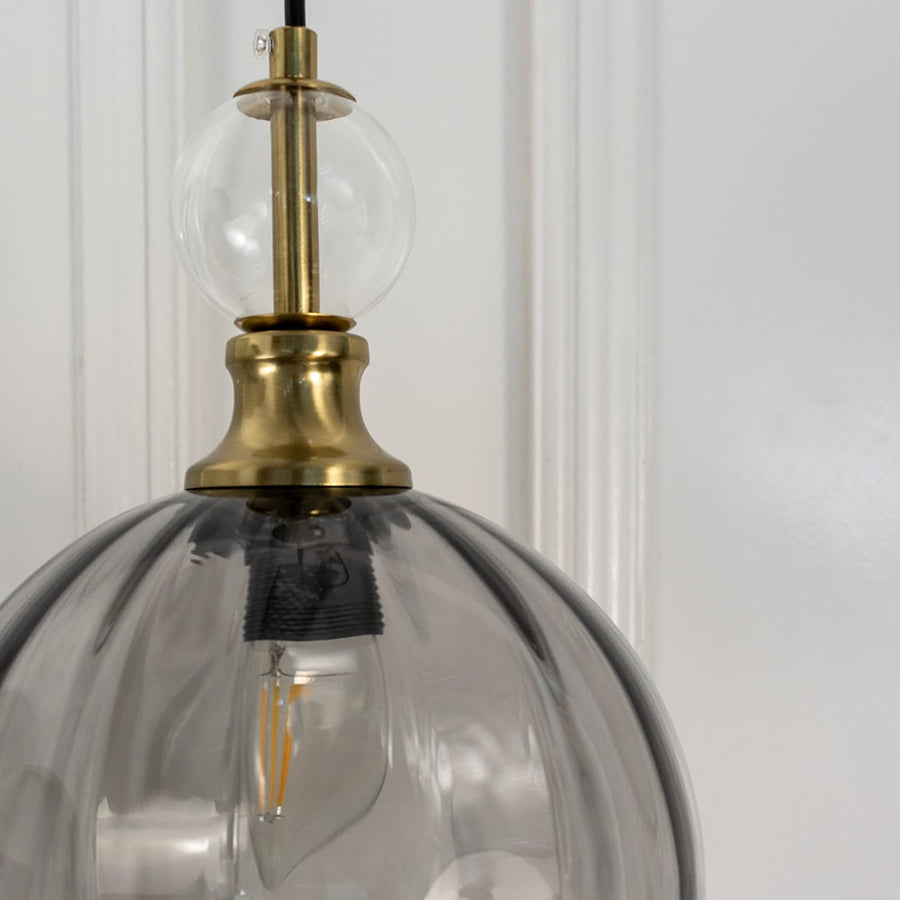 Closeup of smoky grey glass pendant light with antique brass hardware showcasing premium craftsmanship.