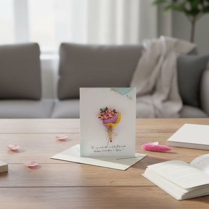 A handmade mini flower bouquet greeting card standing on a wooden living room coffee table in front of a blurry grey couch.