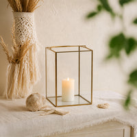 Elegant gold brass geometric glass lantern frame holding a white candle styled on a textured beige living room sideboard.