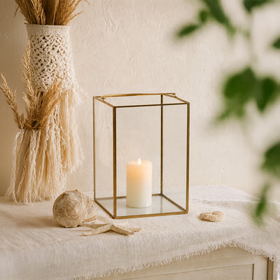 Elegant gold brass geometric glass lantern frame holding a white candle styled on a textured beige living room sideboard.