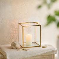 Elegant gold brass geometric glass lantern frame holding a lit white candle styled on an entryway console tabletop setup.
