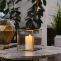 Modern gold brass geometric glass lantern frame with a glowing white candle placed on a luxury marble coffee table top.