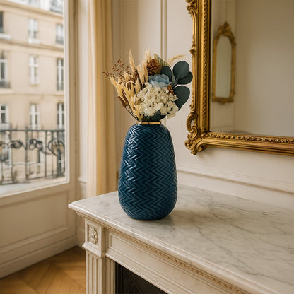 Blue zigzag ceramic vase with gold rim styled with dried floral arrangement placed on a marble console in an elegant living space.