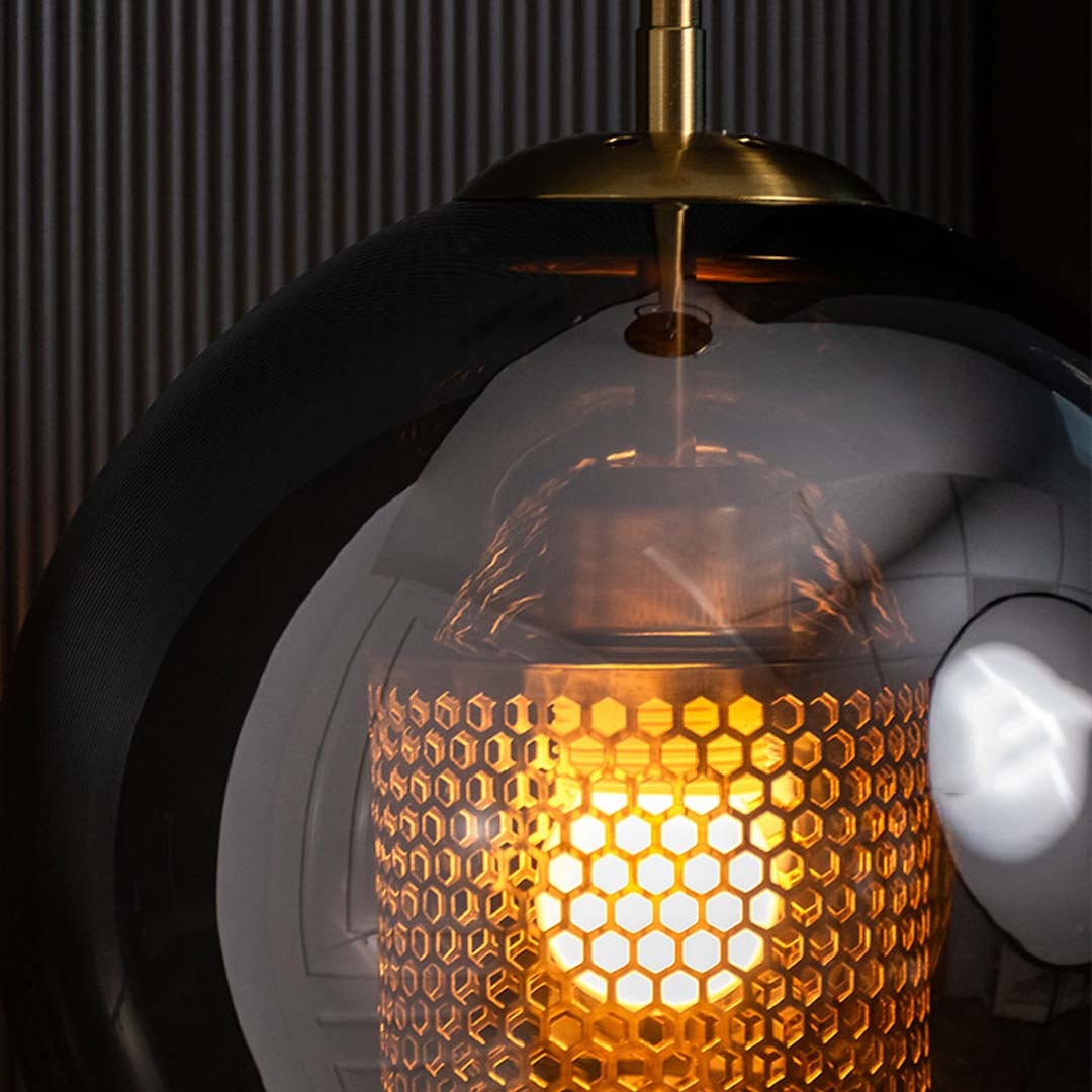 Closeup view of the smoky glass globe pendant light showing its reflective surface brass detailing and patterned inner mesh shade.