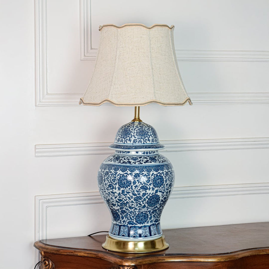 Classic blue white ceramic table lamp with ornate floral design brass base and fabric shade on off white background.