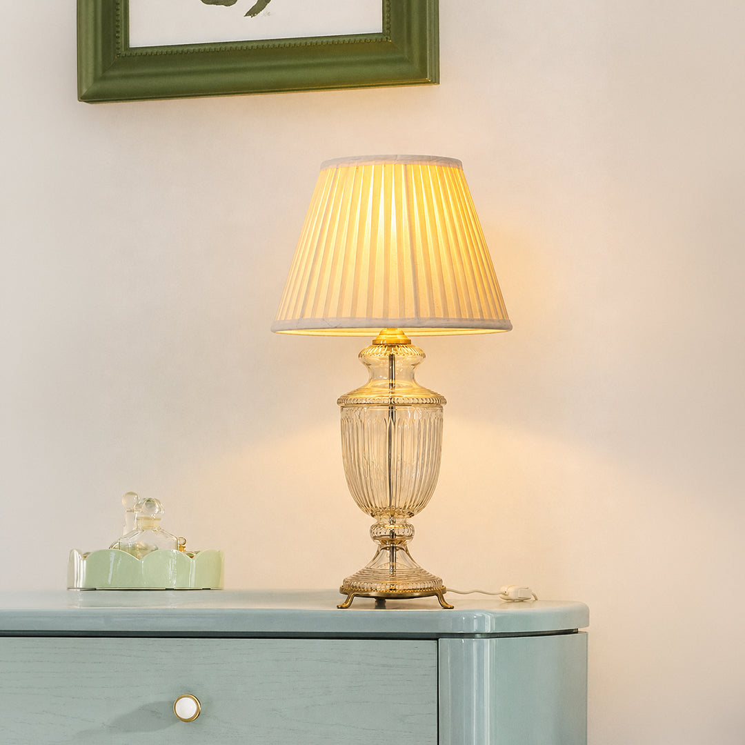 Clear etched glass table lamp with pleated fabric shade displayed on a sideboard creating elegant traditional ambient lighting.