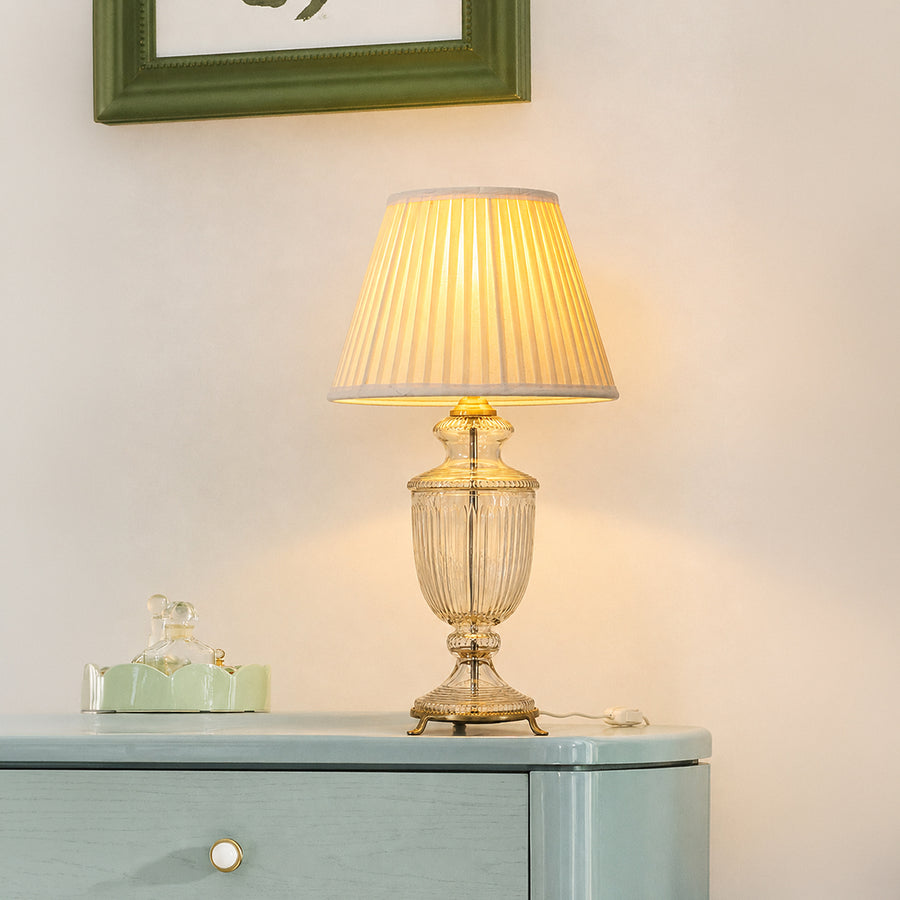 Clear etched glass table lamp with pleated fabric shade displayed on a sideboard creating elegant traditional ambient lighting.