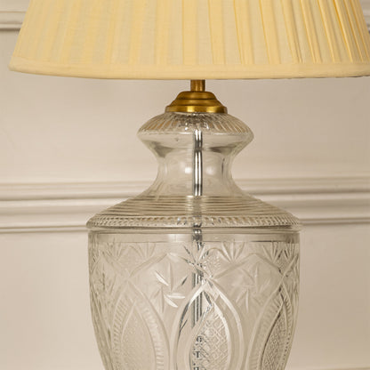 Clear etched glass table lamp showcasing intricate cut glass craftsmanship with brass accents and pleated fabric shade.