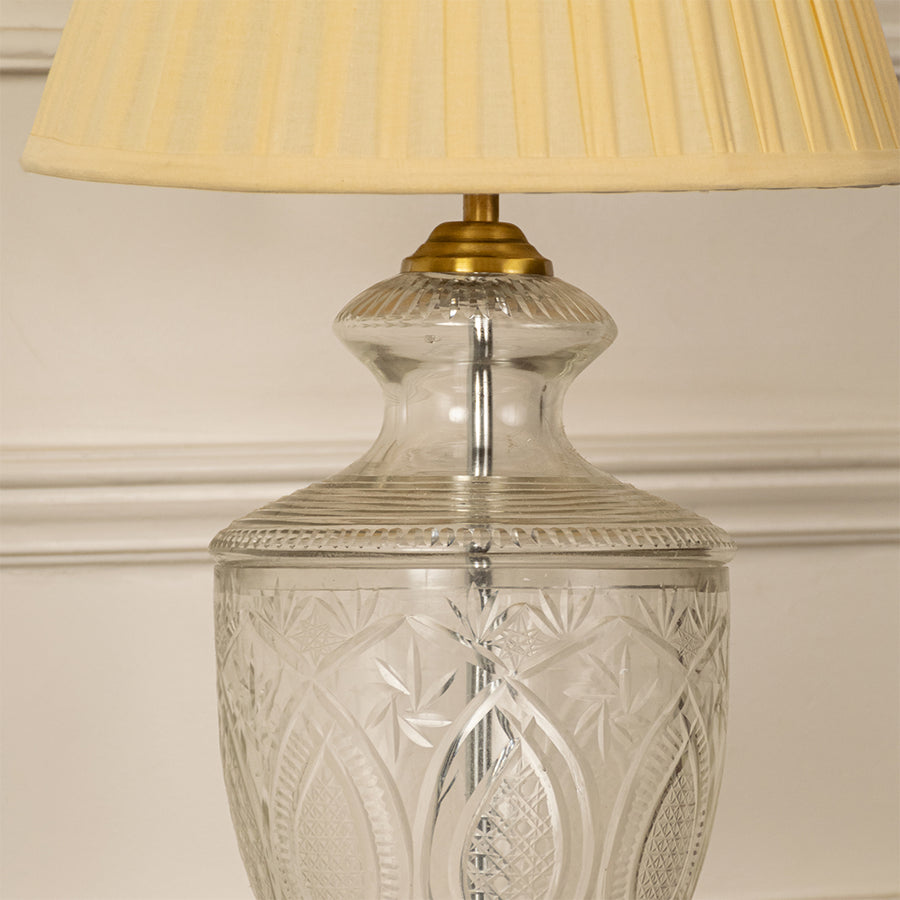Clear etched glass table lamp showcasing intricate cut glass craftsmanship with brass accents and pleated fabric shade.