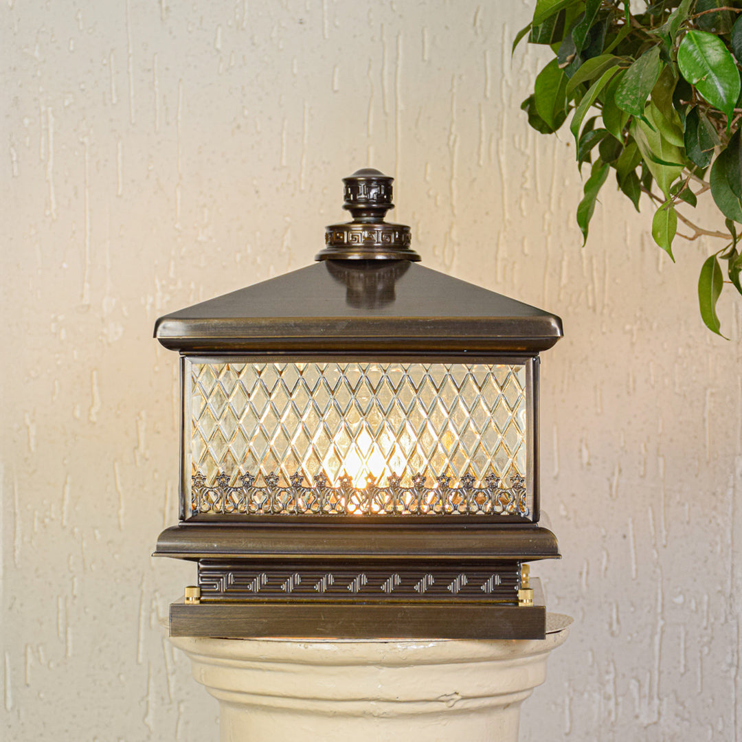 Outdoor pillar light with bronze metal frame and patterned glass shade mounted on exterior wall ideal for garden or patio lighting.